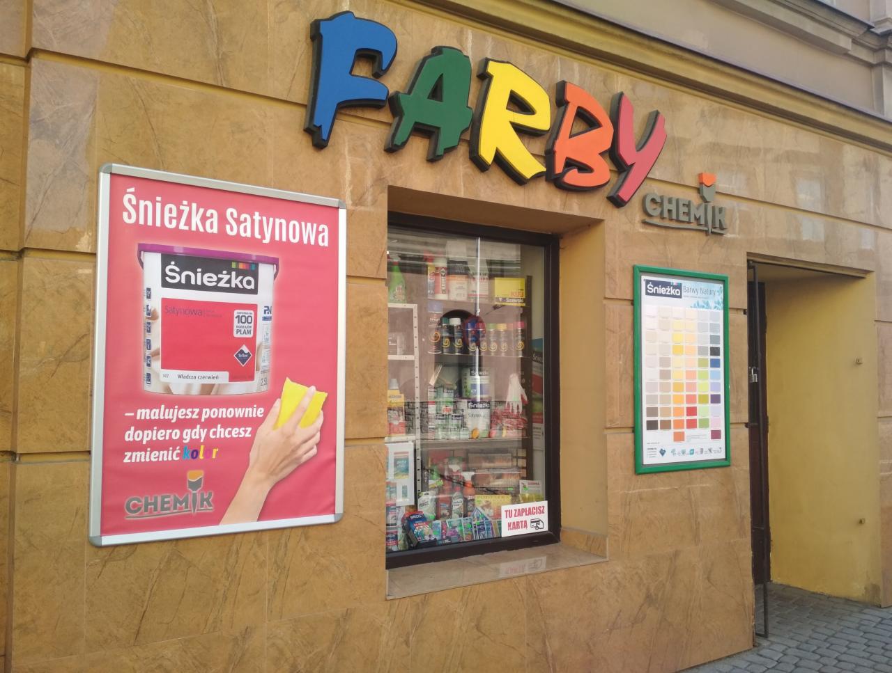 Fasada sklepu z farbami z szyldem 'FARBY CHEMIK', okno wystawowe z produktami, plakat reklamowy farby Śnieżka Satynowa i wzornik kolorów Śnieżka Barwy Natury.