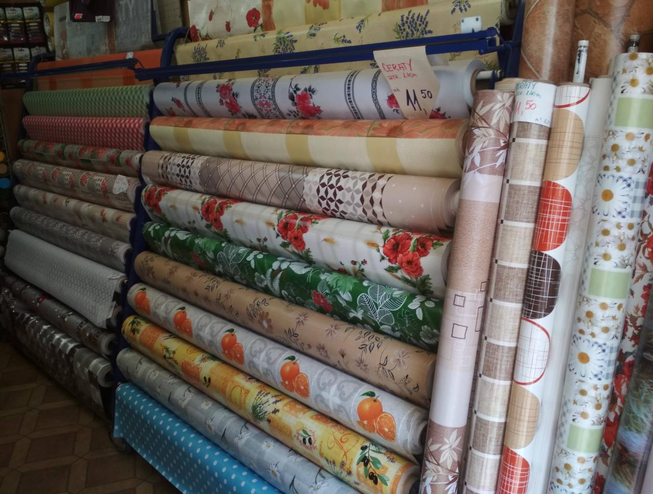 Rzędy rolek cerat z różnorodnymi wzorami, od kwiatowych po geometryczne i owocowe, ułożone na metalowym regale w sklepie.