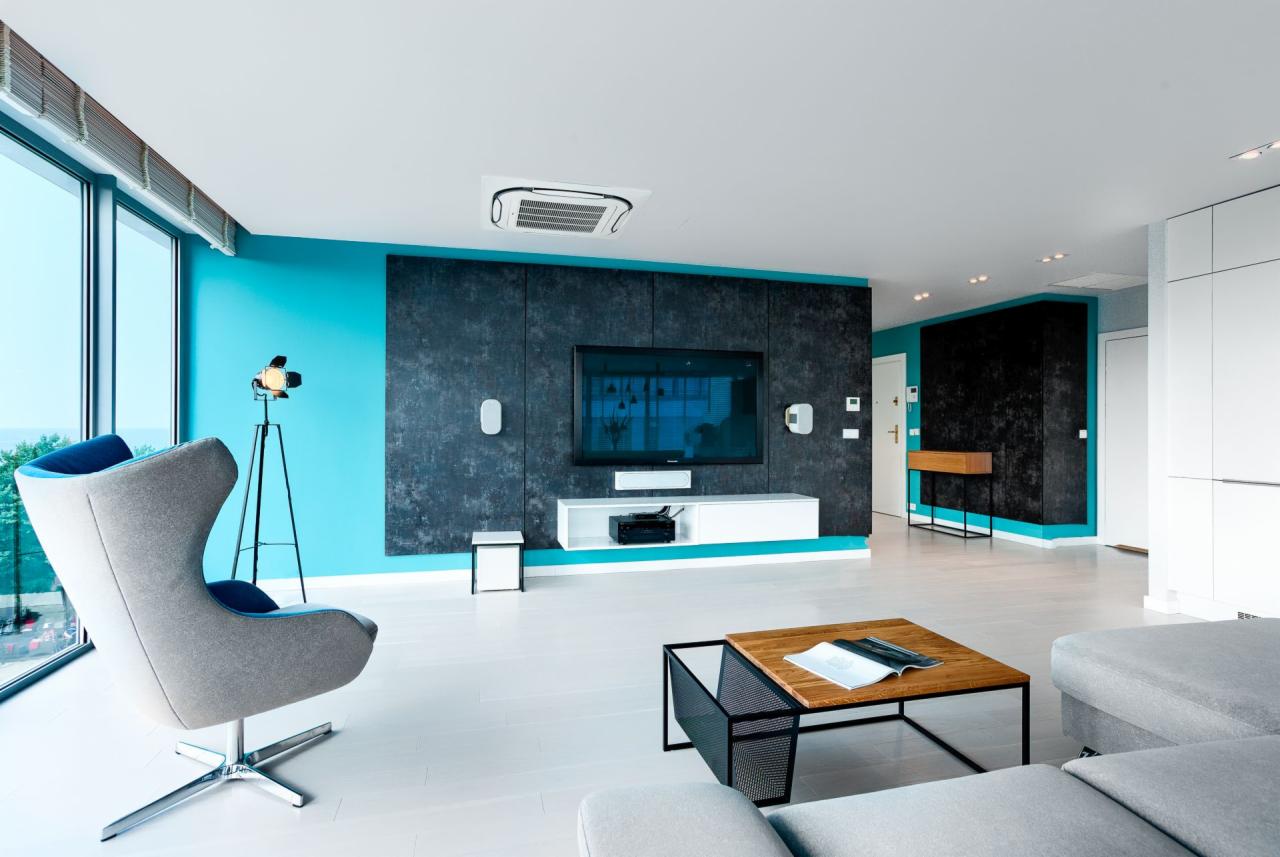 Nowoczesny salon z turkusowymi ścianami, ciemnoszarą ścianą TV, designerskim fotelem i drewnianym stolikiem kawowym z magazynem.