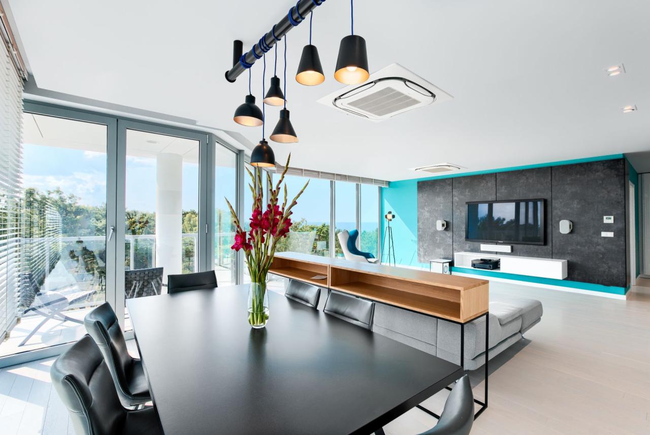 Nowoczesny salon z dużym oknem balkonowym, czarnym stołem jadalnym, wiszącymi lampami na rurze i ścianą telewizyjną z turkusowym akcentem.