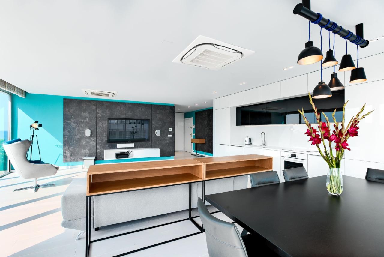 Nowoczesne, jasne wnętrze apartamentu z turkusową ścianą, szarą sofą, drewnianymi półkami i czarnym stołem jadalnym z bukietem czerwonych mieczyków.