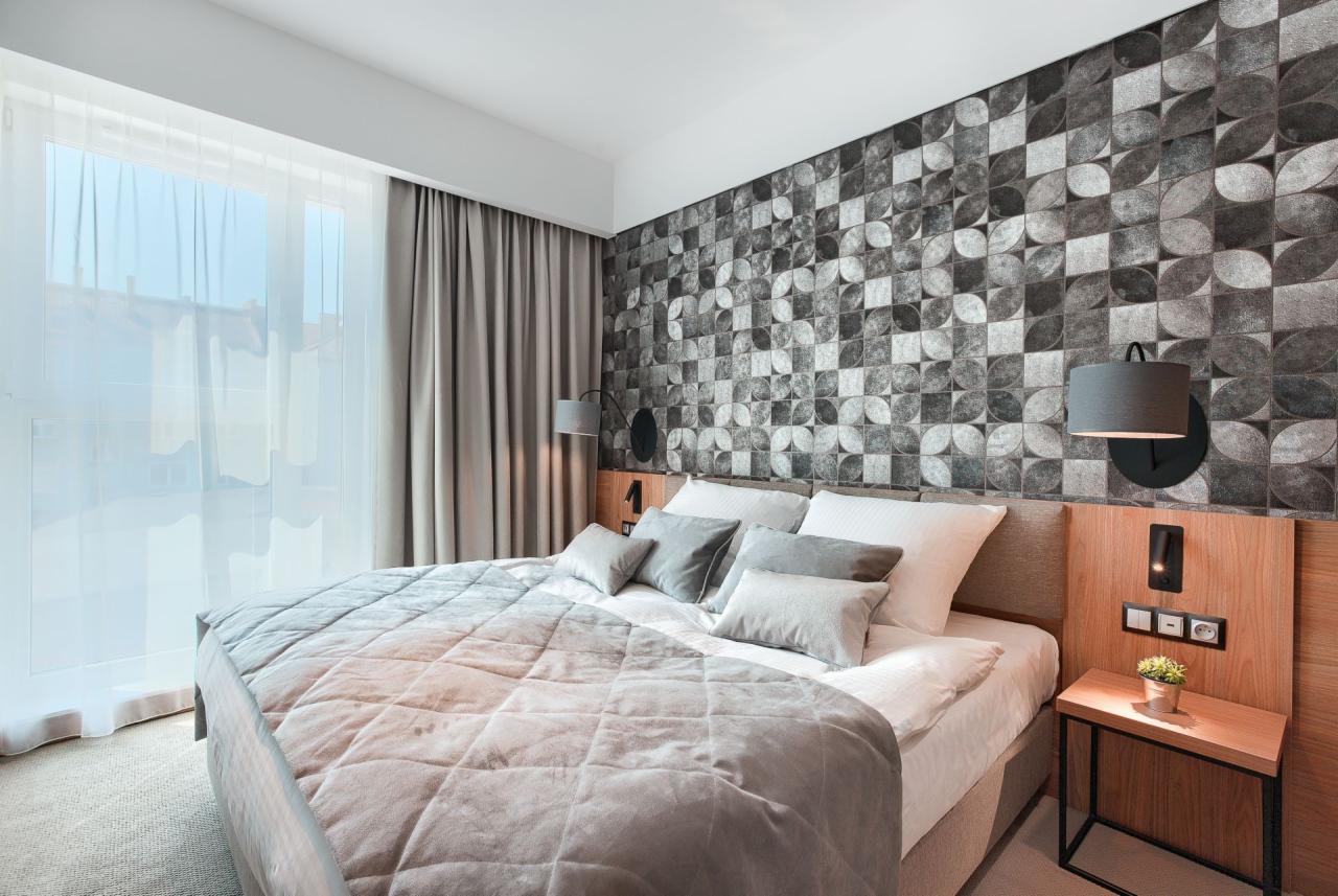 Nowoczesna sypialnia z łóżkiem w odcieniach szarości, geometryczną tapetą i minimalistycznymi lampkami nocnymi