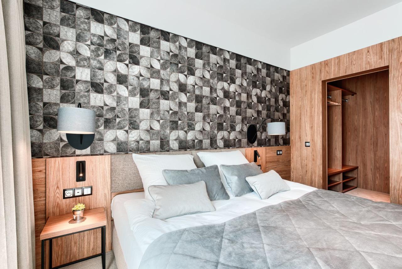 Nowoczesna sypialnia z tapetą w geometryczne wzory, szarą pościelą i drewnianą zabudową szafy wnękowej.