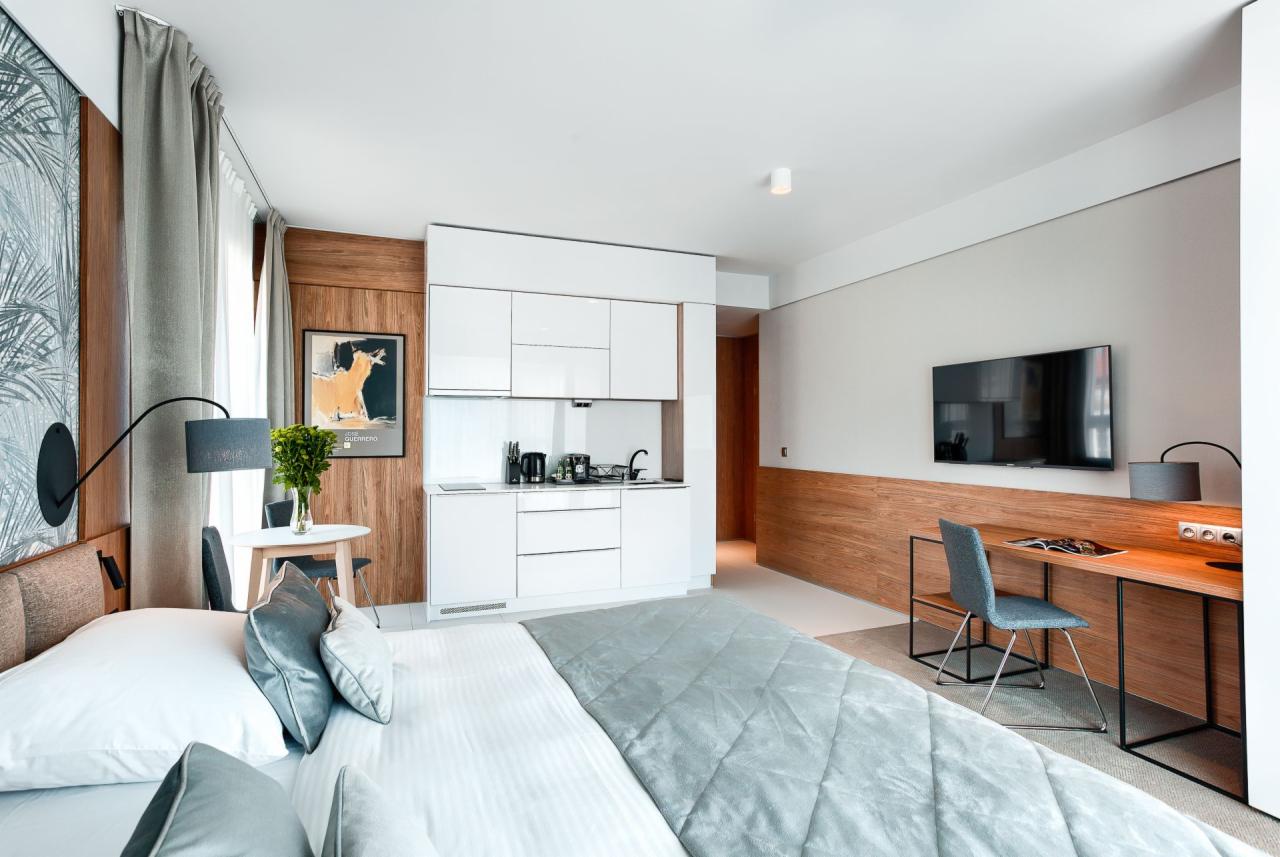 Nowoczesne studio z aneksem kuchennym, biurkiem i łóżkiem, akcenty z drewna, plakat z motywem zwierzęcym nad okrągłym stolikiem.