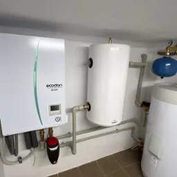 Zamontowana jednostka wewnętrzna pompy ciepła Mitsubishi Ecodan z podłączonymi zbiornikami buforowymi i osprzętem hydraulicznym w pomieszczeniu technicznym.