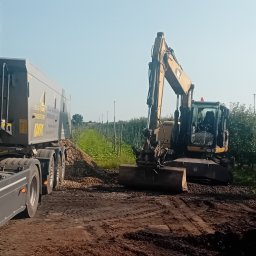 Bartek Lenarczyk - Ciężarówka z naczepą i koparka na tle sadu. Koparka wyrównuje teren, a ciężarówka czeka na załadunek. Widoczne ślady opon na ziemi.