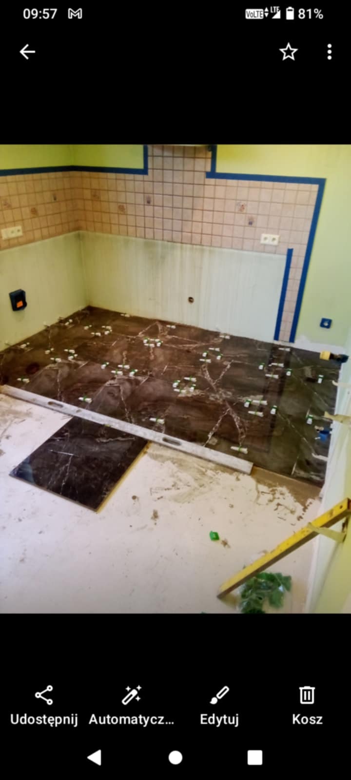 Układanie brązowych płytek podłogowych z marmurkowym wzorem w łazience. Widoczne poziomice i krzyżyki dystansowe. Częściowo ułożona podłoga.