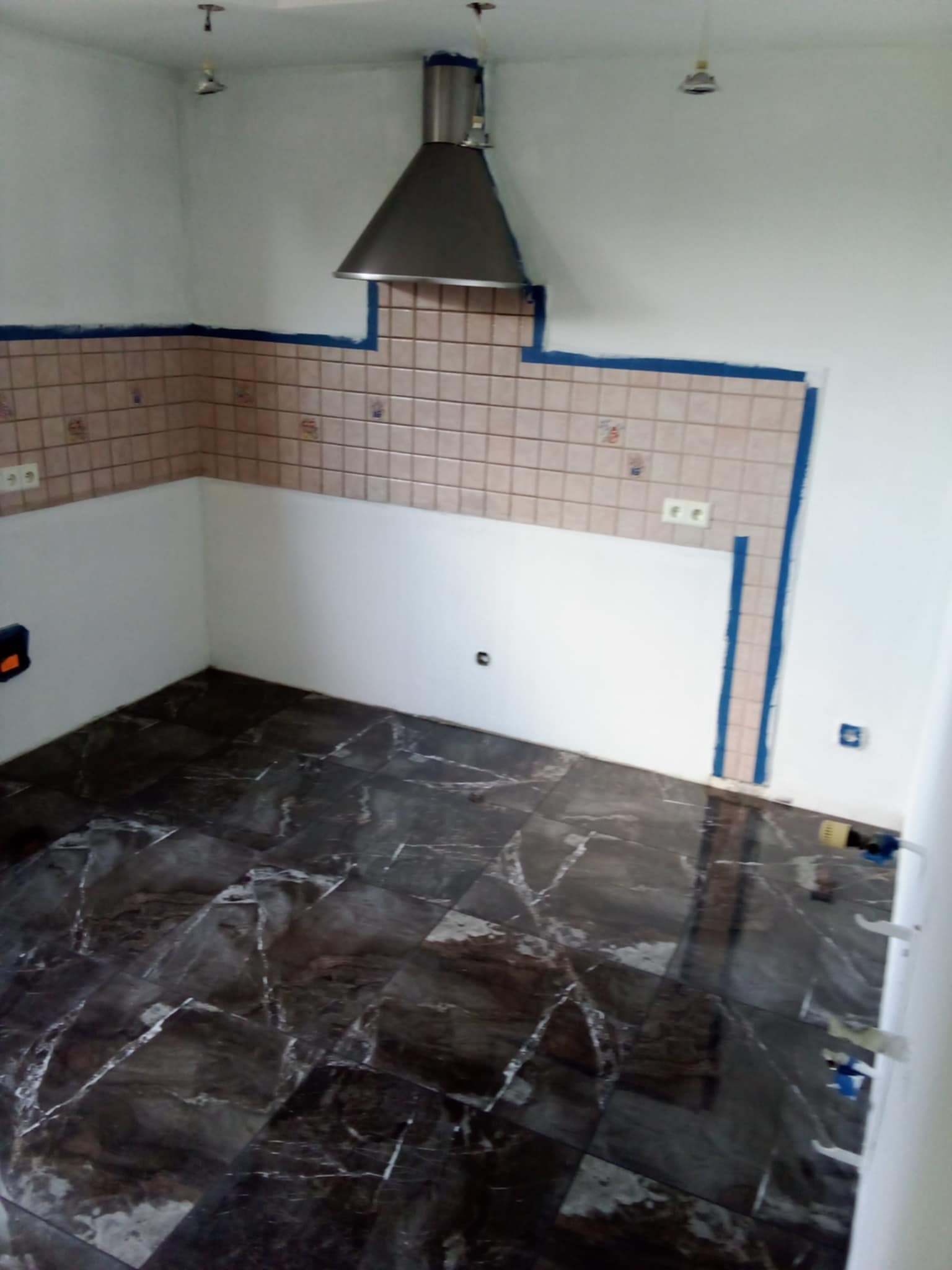 Kuchnia w trakcie prac wykończeniowych: położona podłoga z płytek imitujących marmur, częściowo wykończona ściana z beżowych płytek, zabezpieczona taśmą malarską.