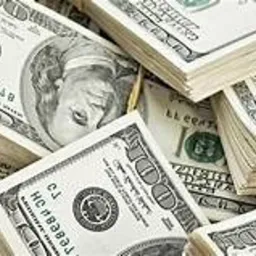 Stosy banknotów studolarowych, spięte gumkami recepturkami, ułożone jeden na drugim pod różnymi kątami, tworzące chaotyczny, ale sugestywny obraz bogactwa i finansów.