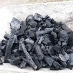 Kupa pociętego na kawałki czarnego drewna w taczce o betonowym wykończeniu.