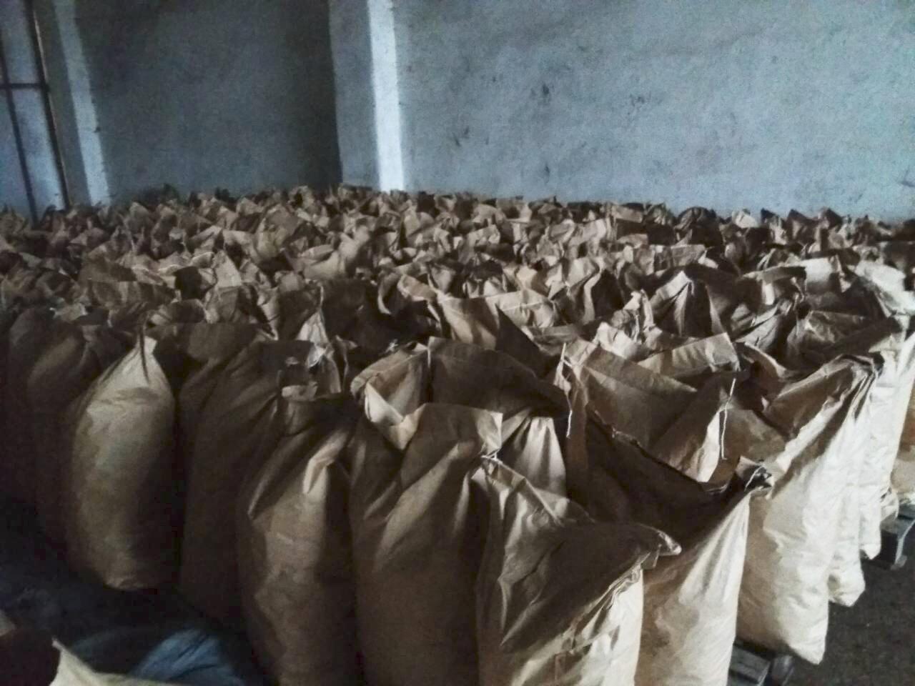 Magazyn pełen worków z materiałem opałowym, ułożonych na paletach, widoczne ściany magazynu z efektem starego betonu.