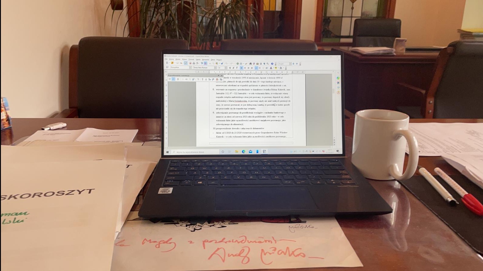 Biuro: laptop z dokumentem prawnym na biurku, obok kubek i długopisy. Na pierwszym planie teczka z napisem 'SKOROSZYT' i odręczne notatki.