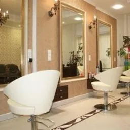 Eleganckie wnętrze salonu z trzema lustrami w złotych ramach, beżowe ściany z wzorzystą tapetą, białe, obrotowe fotele i marmurowa podłoga z ciemnym, dekoracyjnym pasem.