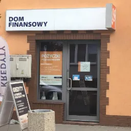 Fasada budynku 'Dom Finansowy' z szyldem nad wejściem, obok reklama kredytów gotówkowych i pozabankowych, flaga reklamowa. Widoczne informacje o RRSO i maksymalnym okresie spłaty.