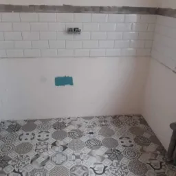 Wnętrze w trakcie remontu: ułożona wzorzysta podłoga z płytek, białe płytki na ścianie częściowo położone, widoczne instalacje wodne.