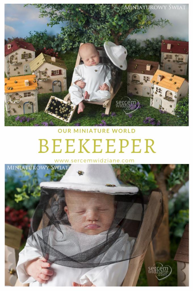 Śpiący noworodek w kostiumie pszczelarza, leżący na miniaturowym leżaku, otoczony miniaturowymi domkami dla pszczół i ramką z pszczołami, w scenerii imitującej ogród.