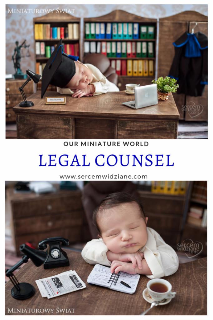 Niemowlę w todze i birecie śpiące na miniaturowym biurku z atrybutami prawnika: laptopem, lampką, filiżanką herbaty i tabliczką z imieniem, stylizowane na sesję biznesową.