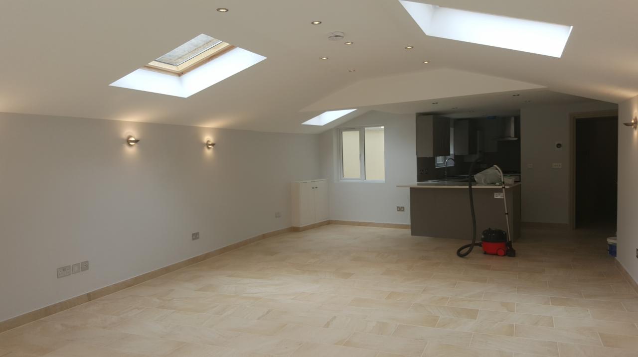Wnętrze po remoncie: jasna podłoga z płytek, świeżo pomalowane ściany, okna dachowe i zabudowa kuchenna w tle, widoczny odkurzacz.