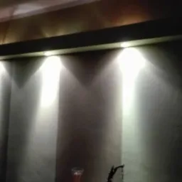 Ściana z oświetleniem punktowym LED, dekoracyjny gzyms, stolik z kieliszkiem, zegarem i wazonem.