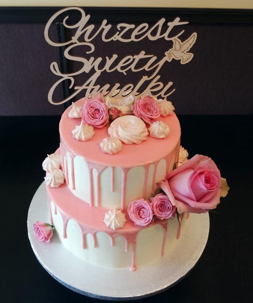 Dwupiętrowy tort z białym kremem, różowym lukrem, różami i bezami, z drewnianym topperem 'Chrzest Święty Aniołki' z gołębiem.