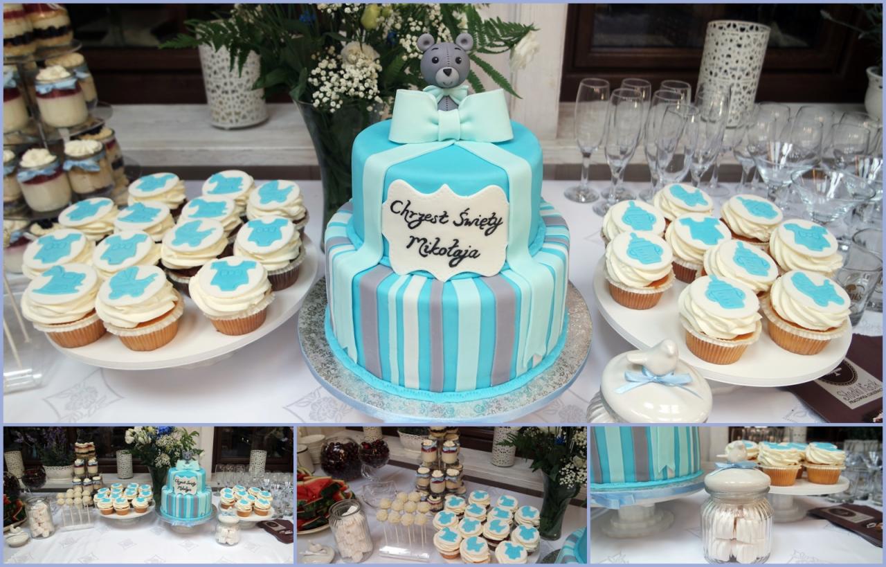 Dwupoziomowy tort w odcieniach błękitu i szarości, udekorowany napisem 'Chrzest Święty Mikołaja' i misiem na szczycie, otoczony babeczkami z niebieskimi aplikacjami dziecięcych ubranek, ustawiony...