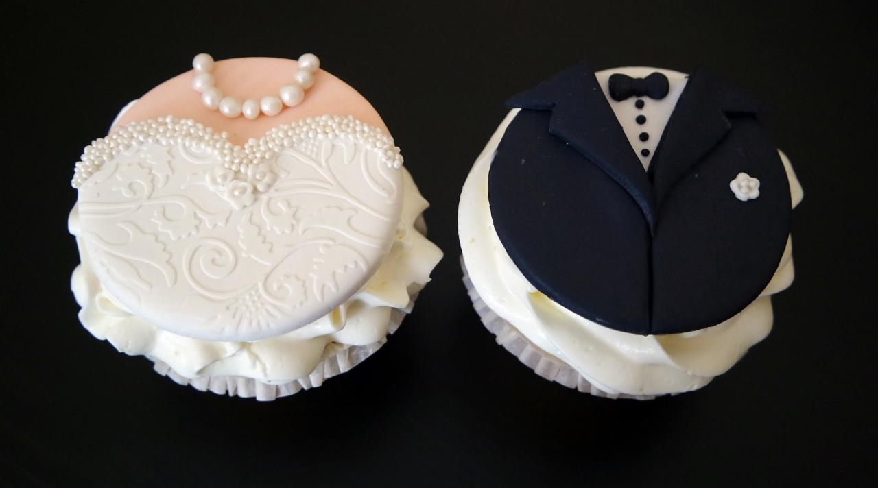 Dwa babeczki: jedna dekorowana jako suknia panny młodej z perłami i koronkowym wzorem, druga jako smoking pana młodego z muszką i butonierką.