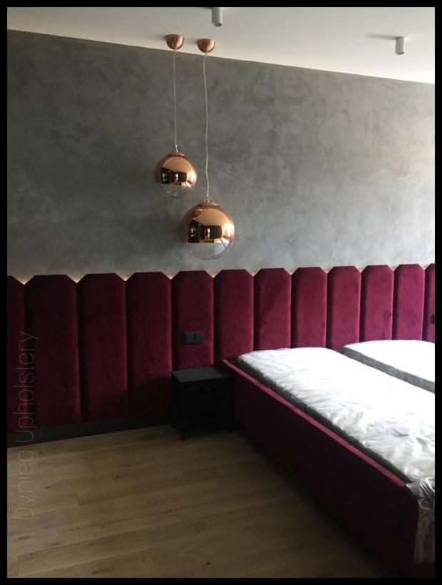Tapicerowane, bordowe panele ścienne za łóżkiem z dwiema lampami wiszącymi w kształcie kul.