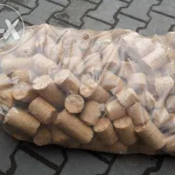 Przezroczysty worek wypełniony cylindrycznymi, jasnobrązowymi peletami z biomasy na szarym brukowanym podłożu.