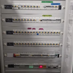 Szara szafa rozdzielcza z wieloma zabezpieczeniami różnicowoprądowymi i nadprądowymi, oznaczona etykietami opisującymi obwody, z diodami LED sygnalizującymi stan pracy.