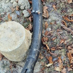 Canad Instalacje elektryczne - Uszkodzony, gruby kabel elektryczny z widocznymi żyłami (miedziana, niebieska) leżący na ziemi z liśćmi i fragmentami betonu. Widoczne ślady naprawy.