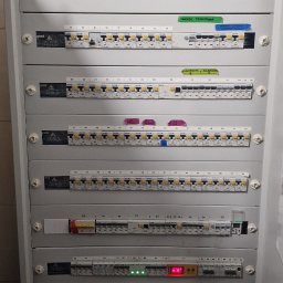 Canad Instalacje elektryczne - Rozdzielnica elektryczna z bezpiecznikami, opisana etykietami, widoczne diody sygnalizacyjne, szara obudowa, pionowy kadr.
