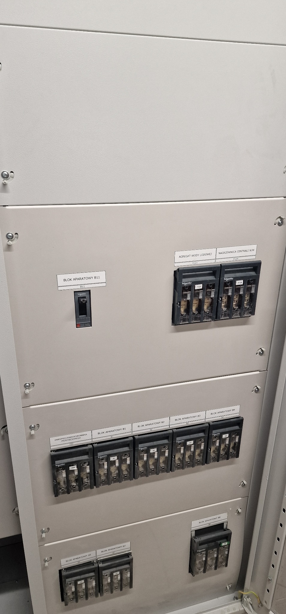 Szara szafa sterownicza z modułami zabezpieczeń i opisami bloków aparatowych B11, B1-B4, B5-B7, agregatu wody lodowej i nagrzewnicy centrali N/W. Widoczne bezpieczniki i okablowanie.