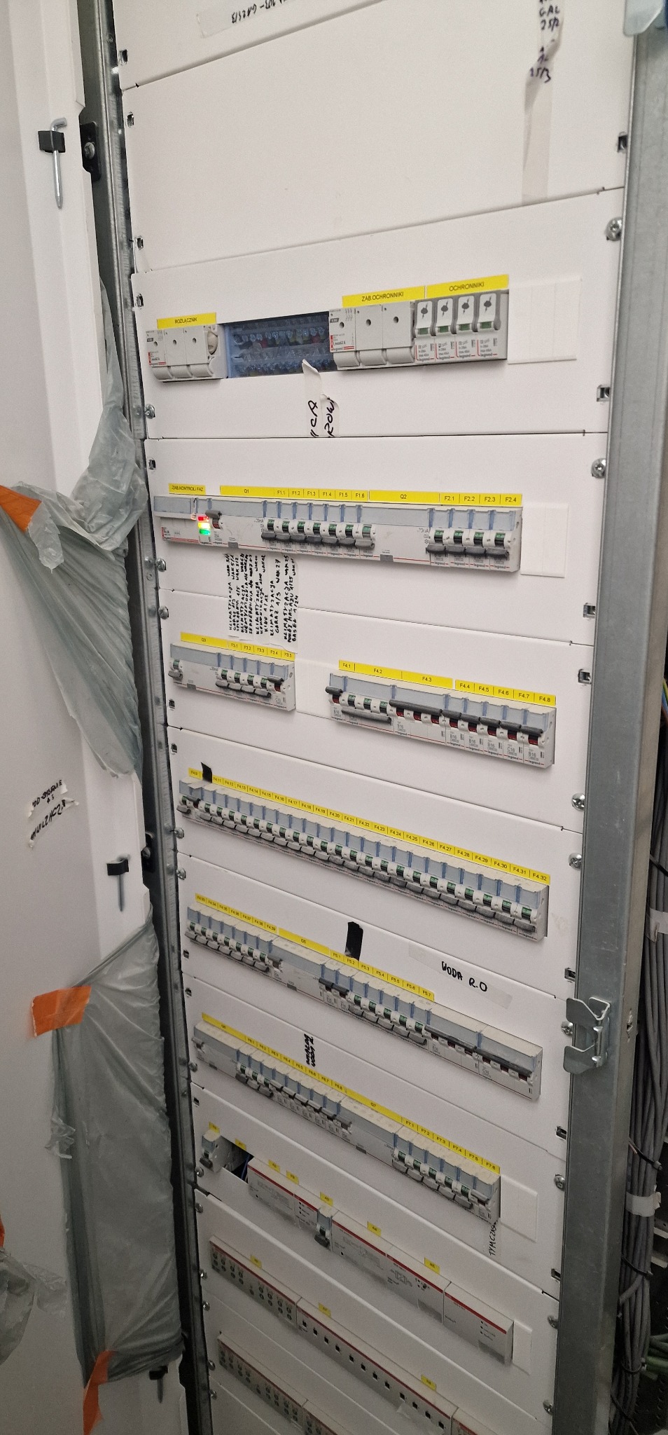 Rozdzielnia elektryczna z licznymi zabezpieczeniami i oznaczeniami, widok z bliska na zamontowane moduły i okablowanie wewnątrz szafy.