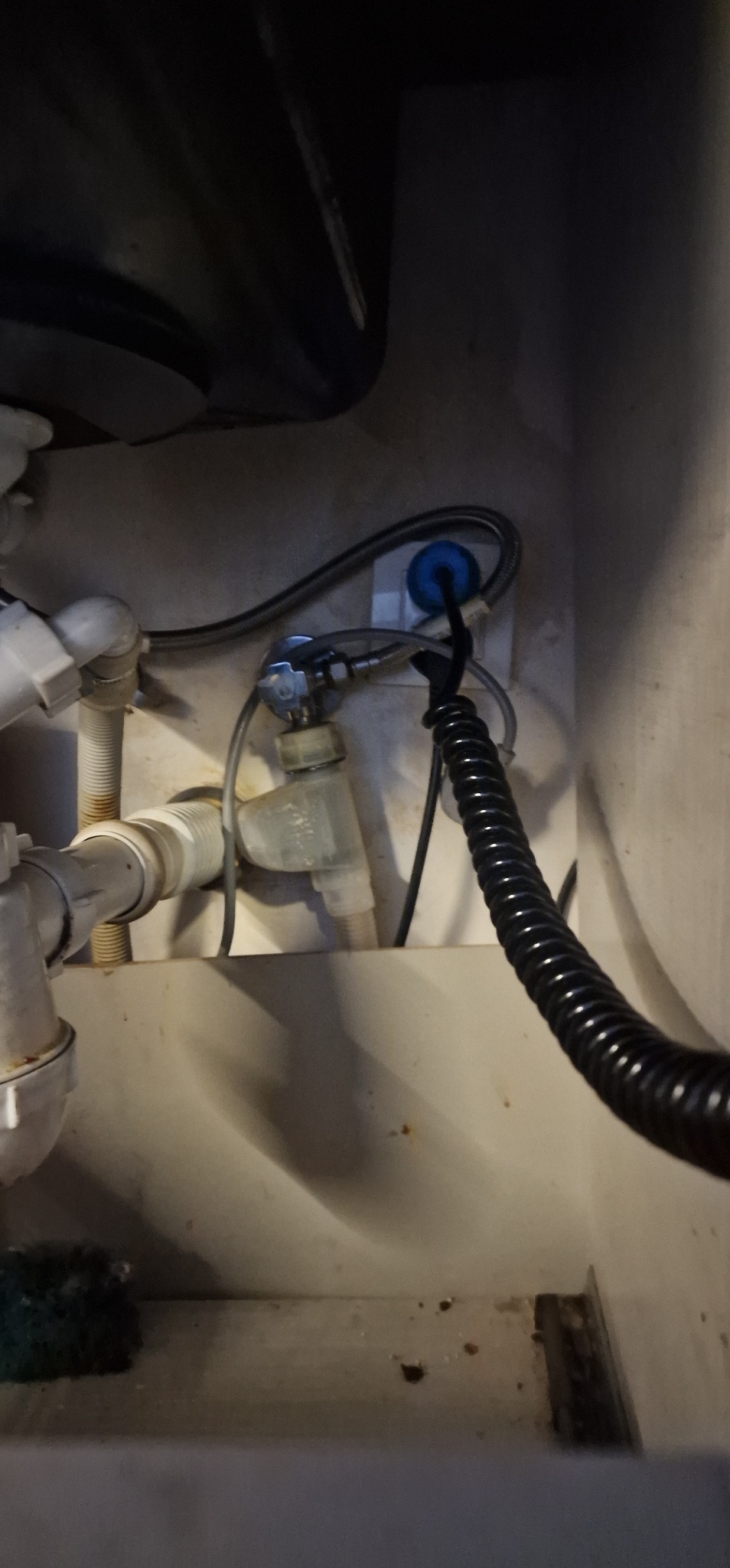 Szczegółowe ujęcie instalacji hydraulicznej pod zlewem, z widocznymi rurami PCV, zaworem odcinającym i elastycznym wężem doprowadzającym wodę.