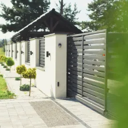 Nowoczesna posesja z przesuwną bramą w kolorze grafitowym, z poziomymi panelami, widoczna z zewnątrz, z elementami małej architektury i zadbaną roślinnością.