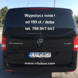 Tył czarnego busa Mercedes Vito Tourer z naklejką reklamową 'Wypożycz mnie! od 199 zł/doba, tel. 798 847 447' na tylnej szybie oraz adresem strony internetowej www.vitobus.com na klapie bagażnika.