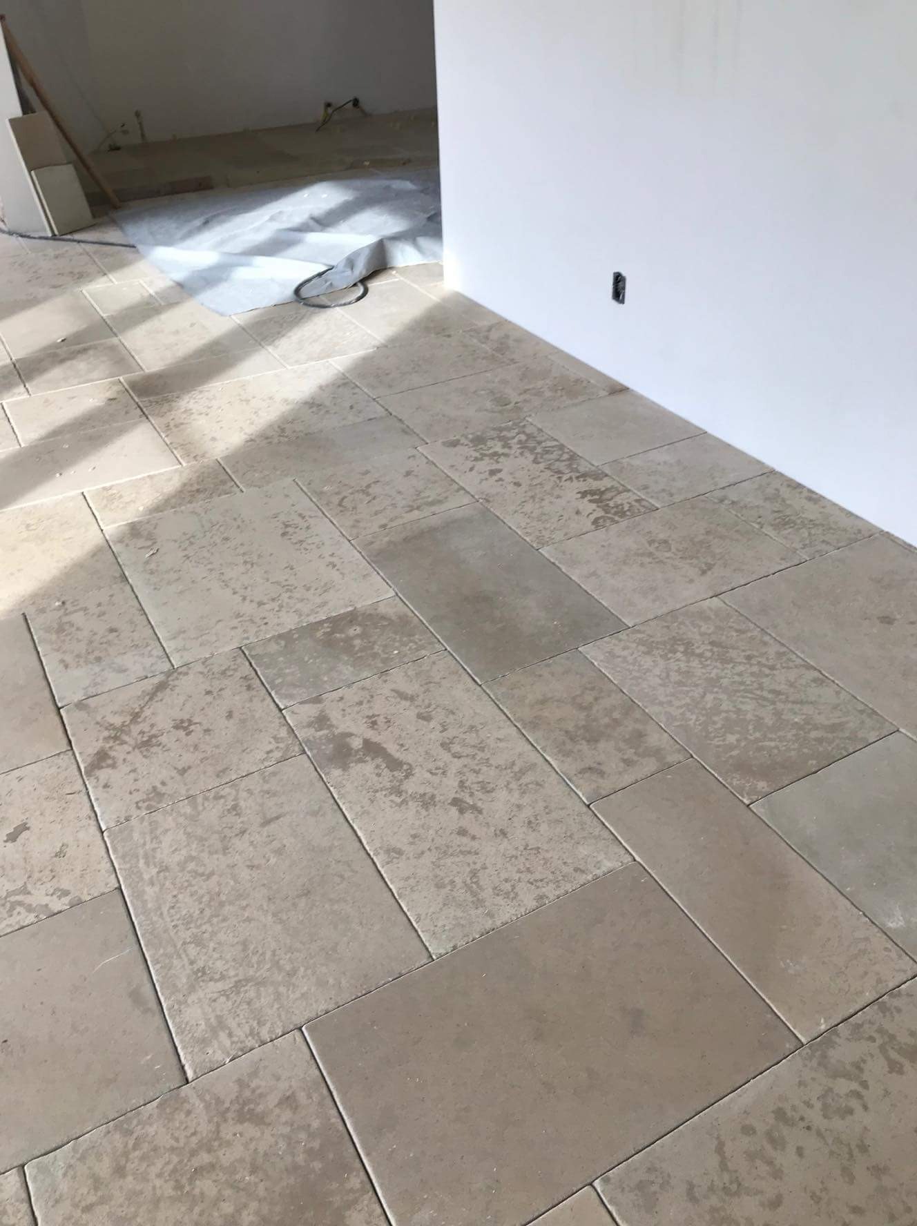 Ułożona podłoga z jasnych, prostokątnych płytek w trakcie prac wykończeniowych, widoczna folia ochronna i niedokończone ściany.