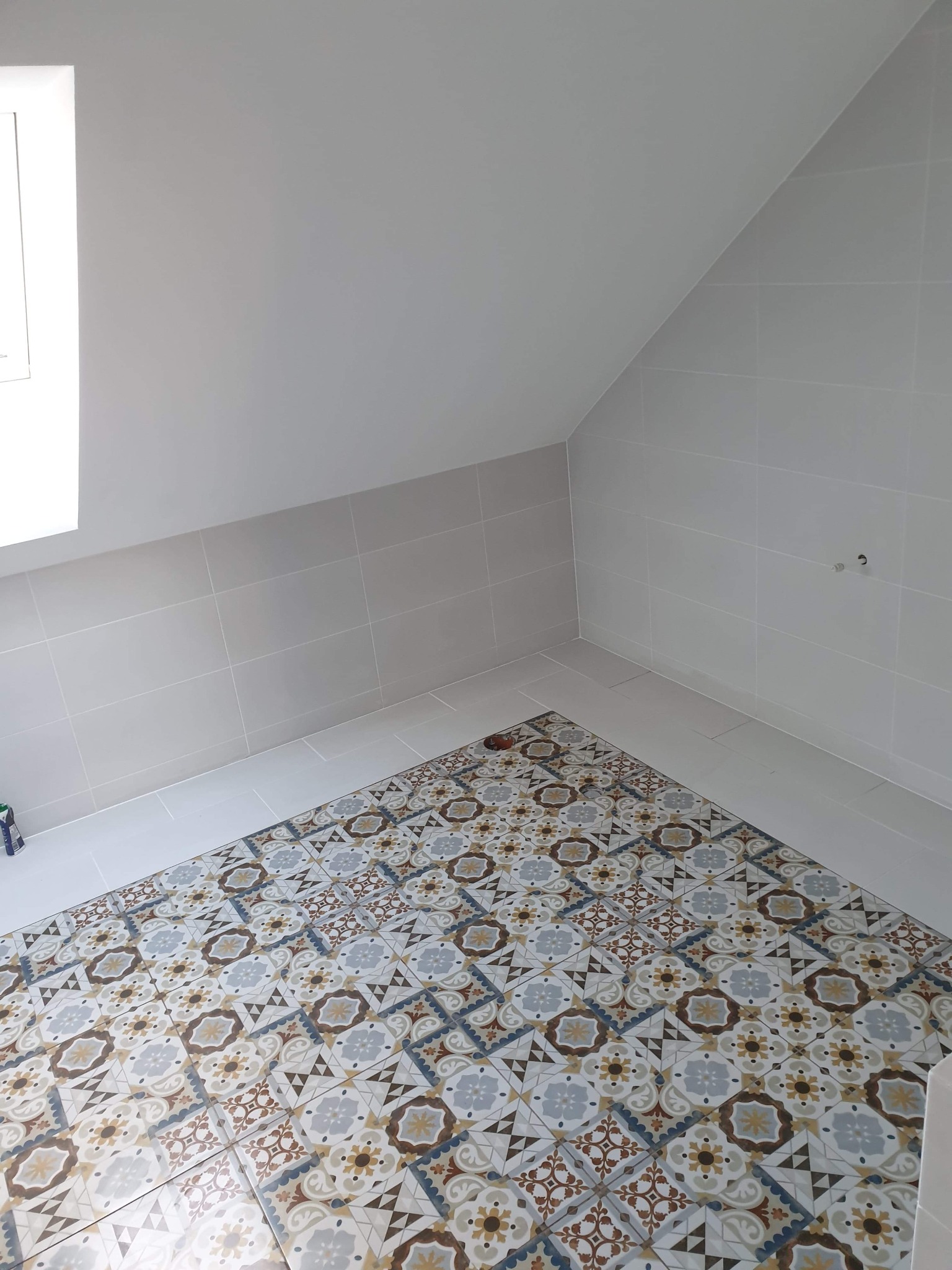 Ukończona łazienka na poddaszu z szarymi płytkami ściennymi i wzorzystą, kolorową podłogą z płytek ceramicznych.