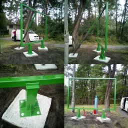 Montaż metalowej konstrukcji ramy pomalowanej na zielono, osadzonej na betonowych fundamentach, widoczne butle z gazem i narzędzia, w tle las i zaparkowany biały bus.