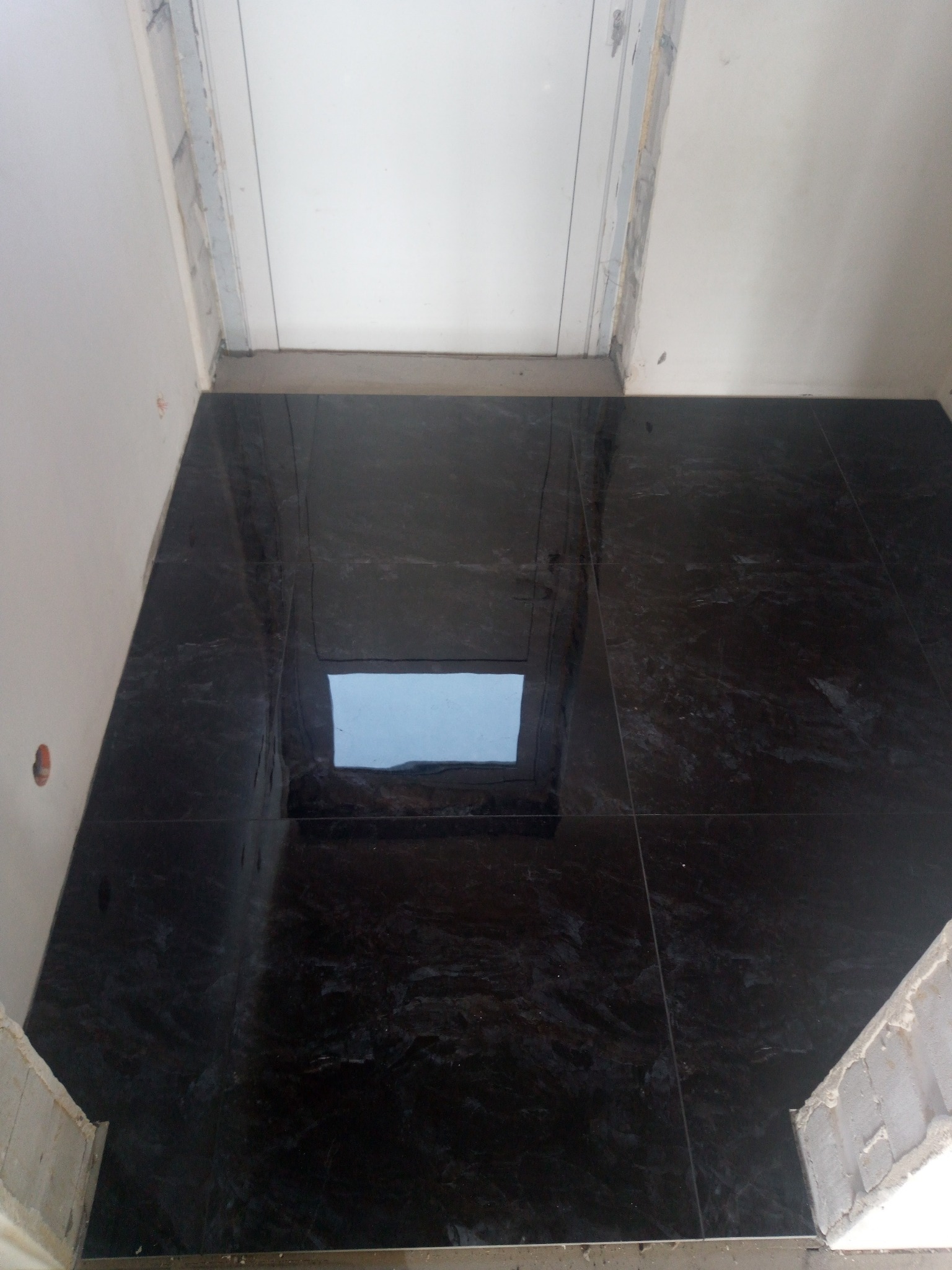 Ułożona, ciemna, marmurkowa podłoga z płytek w pomieszczeniu w trakcie remontu, widoczne ślady po zaprawie na ścianach.