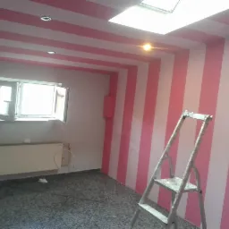 Pokój po remoncie z pomalowanymi ścianami i sufitem w biało-różowe pasy, widoczna drabina malarska, okno i grzejnik