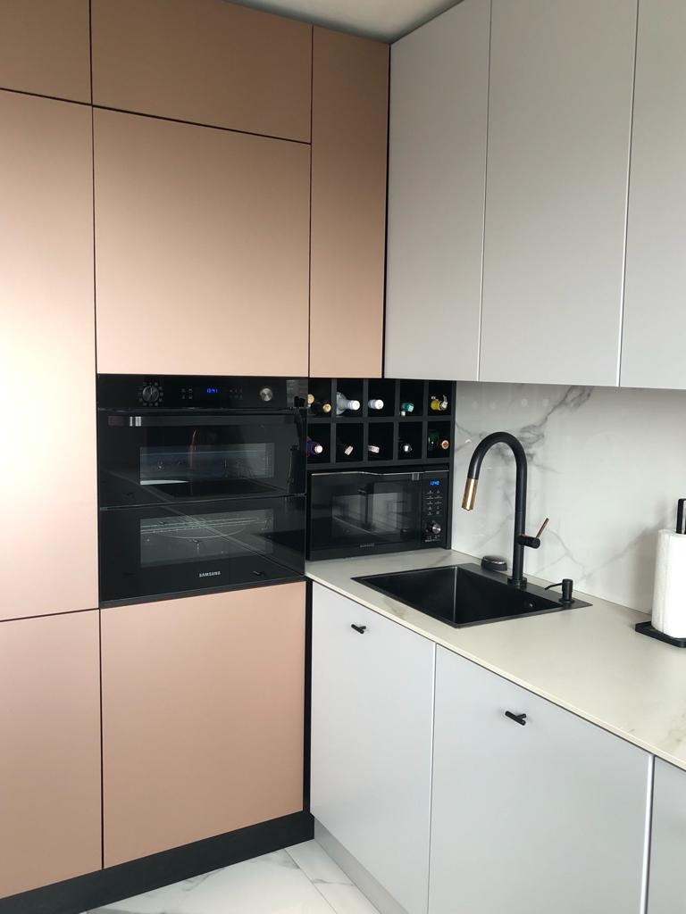 Nowoczesna kuchnia z zabudową w odcieniach różowego złota i szarości, czarną armaturą i wbudowanym regałem na wino.