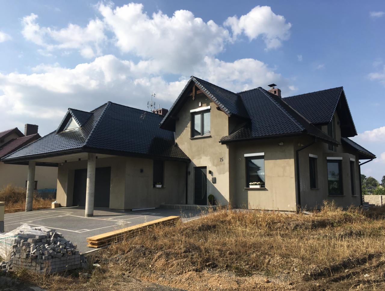 Dom jednorodzinny w Legnicy z nowym, ciemnym dachem i dobudowanym garażem, widoczne materiały budowlane przed budynkiem.