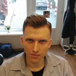 Młody mężczyzna z modną fryzurą po wizycie w salonie fryzjerskim w Bydgoszczy, widok z bliska na twarz i świeżo ostrzyżone włosy.