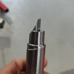 Precyzyjnie obrobiony metalowy trzpień z ostrą krawędzią, trzymany w dłoni, widoczne delikatne ślady obróbki spiralnej.