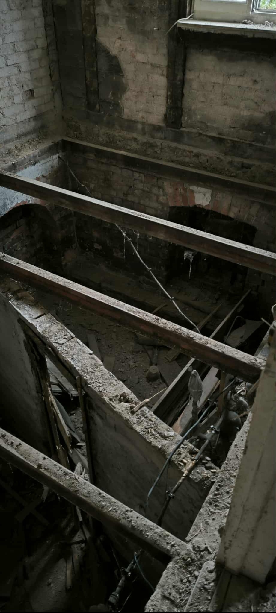 Wnętrze po demontażu podłogi w Wąbrzeźnie. Widoczne stare cegły, drewniane belki stropowe i gruz. Prace rozbiórkowe w trakcie realizacji.