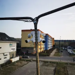 Zestaw czterech kamer przemysłowych Hikvision zamontowany na słupie, widok na parking i budynki mieszkalne w tle.