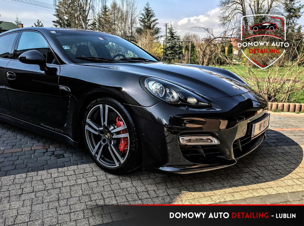Błyszczący, czarny samochód Porsche Panamera GTS po detailingu, z widocznymi czerwonymi zaciskami hamulcowymi i logo firmy detailingowej w prawym górnym rogu.