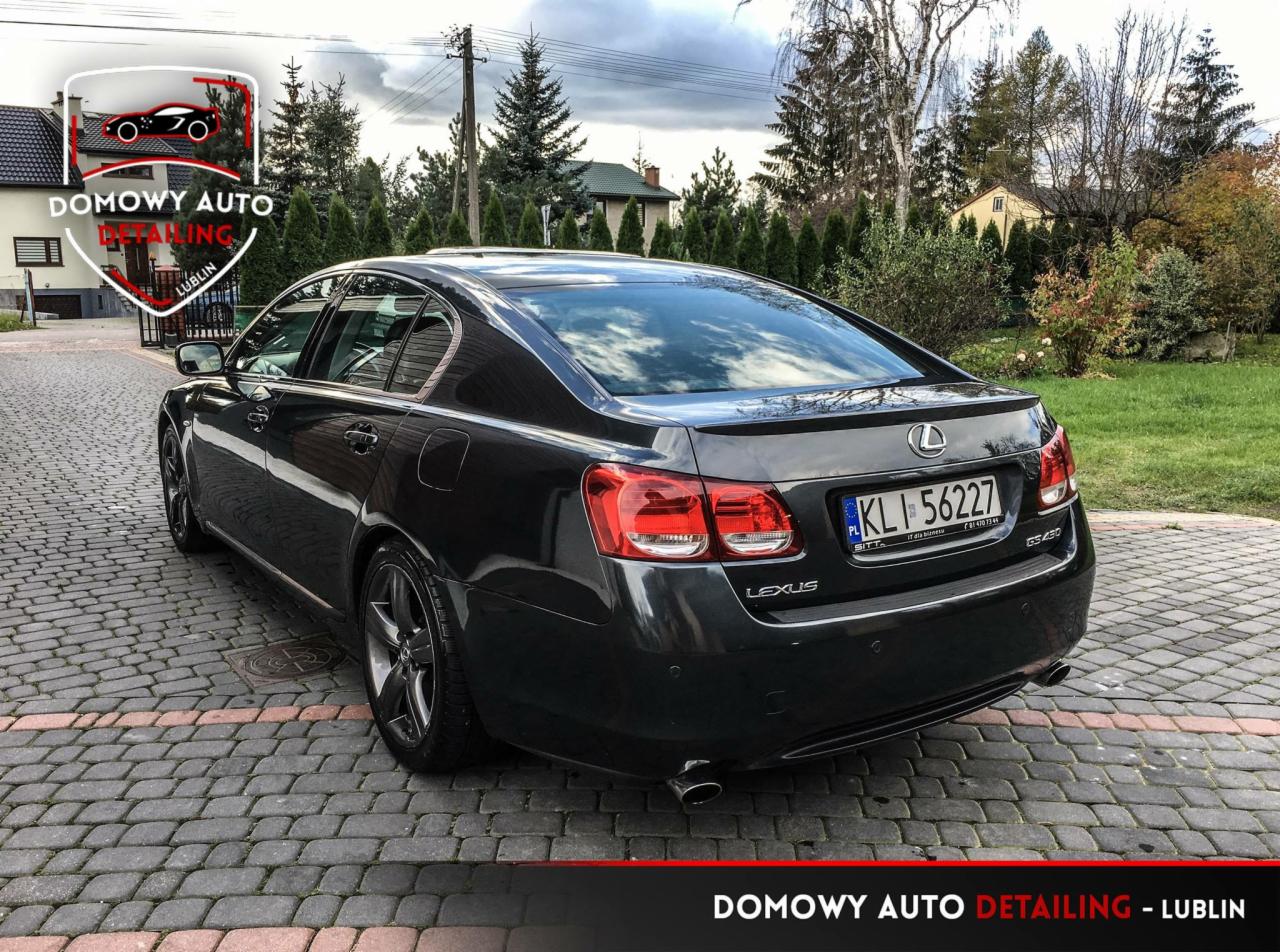 Ciemnoszary Lexus GS 430 po detailingu, widok z tyłu na tle brukowanej nawierzchni i zieleni, z widocznym logo firmy Domowy Auto Detailing Lublin.