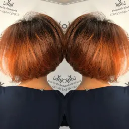 Krótkie, pofalowane włosy z ombre w odcieniach brązu i miedzi, widok z tyłu, odbicie w lustrze, na szyi delikatny srebrny łańcuszek